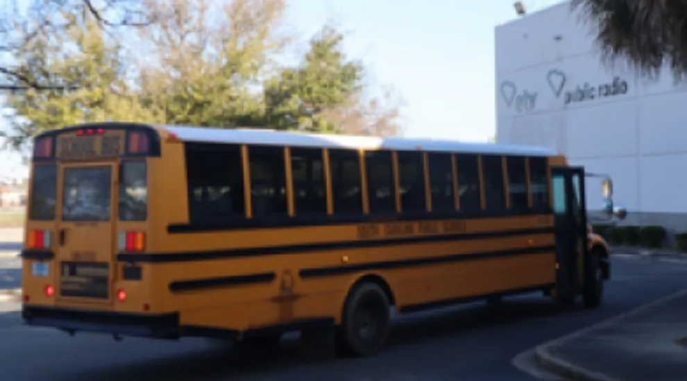 photo of yellow school bus parked in front of SCETV building with SCETV logo and SC Public Radio logo shown in background on building