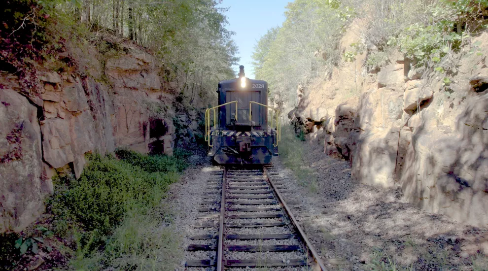 Photo showing the front of a locomotive engine while underway and passing through a narrow canyon