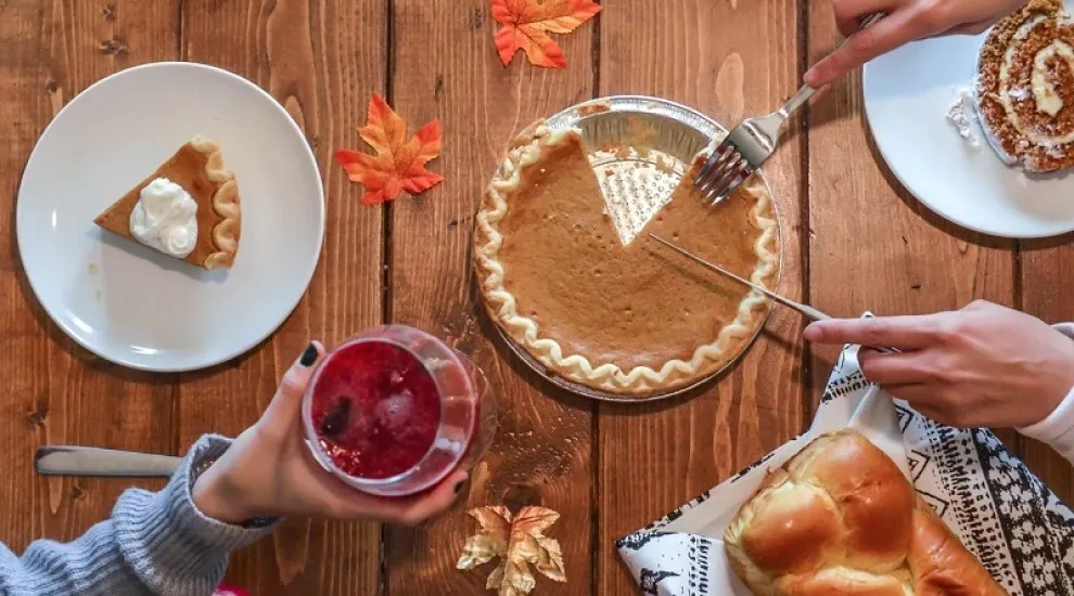 photo of a table scene showing a pumpkin pie, rolls, fall leaves, and more