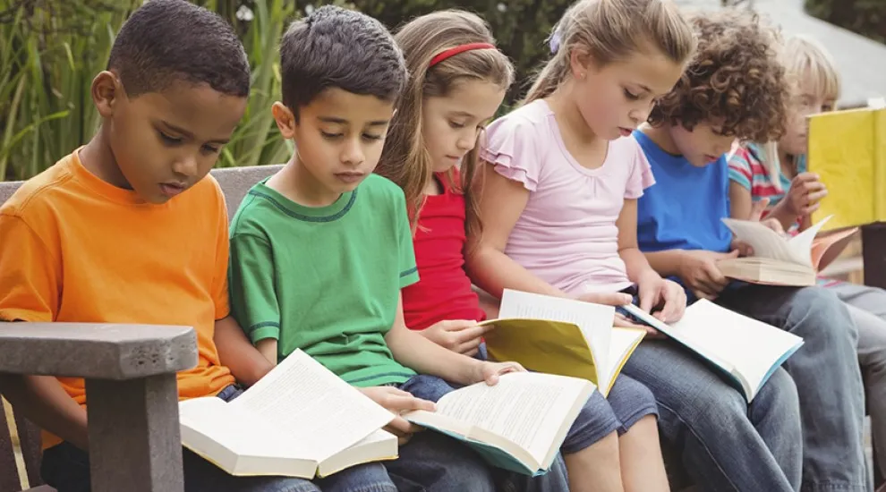 photo of several students sitting on bench reading books