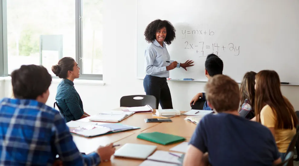 photo of teacher standing at classroom white board with math equations on it in front of seated students