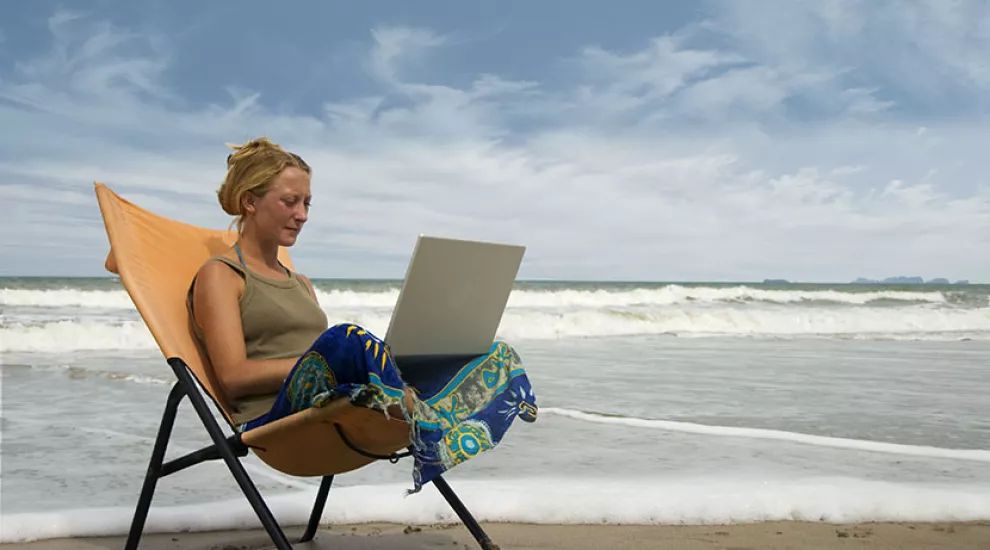 Teacher sitting in chair on beach using laptop