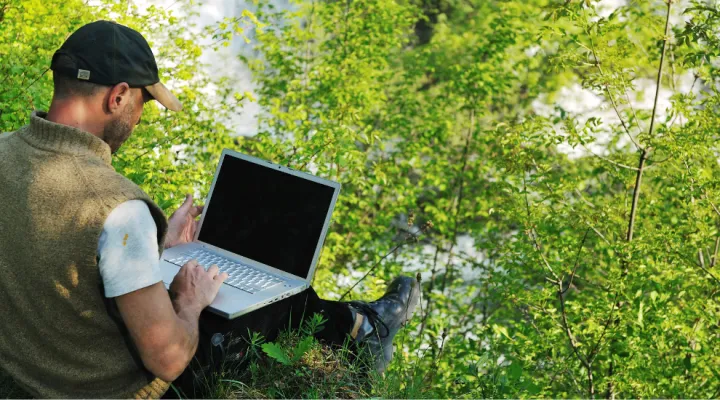photo of man using a laptop outside by the river