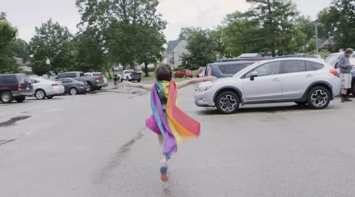 Girl with rainbow cape skips down the street