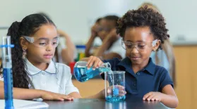 photo of two elementary students working in science class pouring liquid from a beaker while wearing eye safety glasses